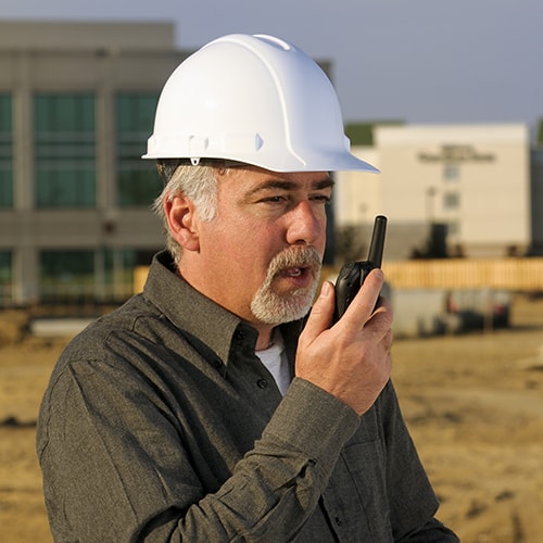 Man in a hard hat using a walkie-talkie on a construction site