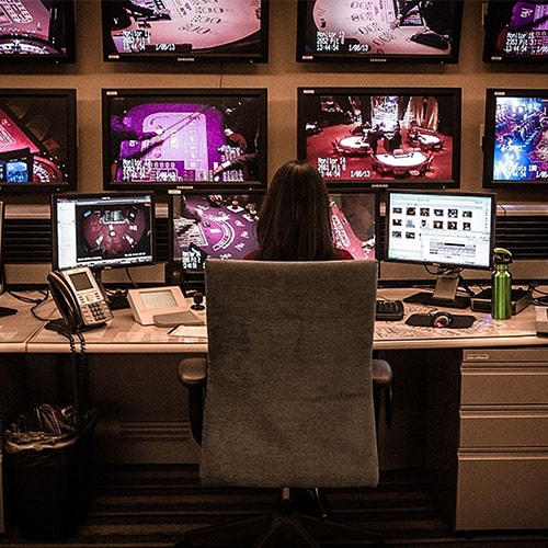 Person sitting at a desk with multiple monitors in a control room setting.