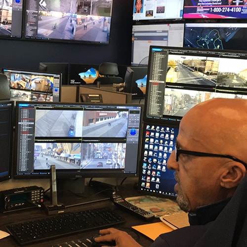 Person monitoring multiple security cameras on computer monitors in a control room.