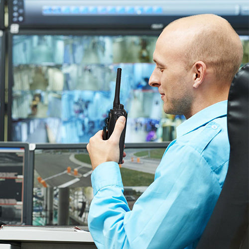 Man in a control room with multiple screens and a walkie-talkie