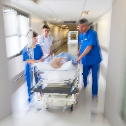 Hospital scene with medical staff moving a patient on a gurney down a hallway.